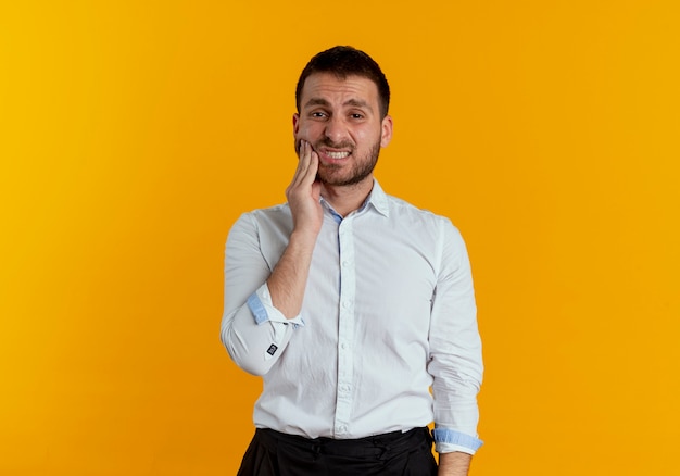 Aching handsome man puts hand on face isolated on orange wall