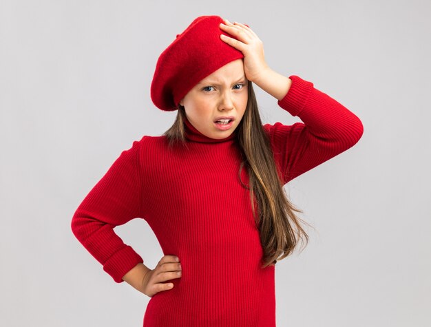 Aching little blonde girl wearing red beret keeping hand on head and on belly  isolated on white wall with copy space