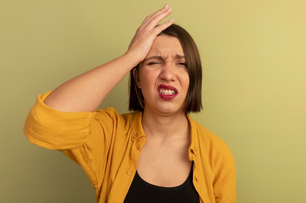 Aching pretty woman puts hand on forehead isolated on olive green wall