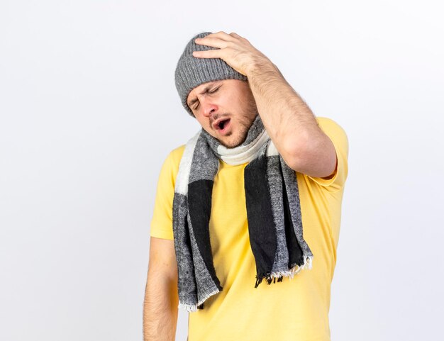 Aching young blonde ill slavic man wearing winter hat and scarf