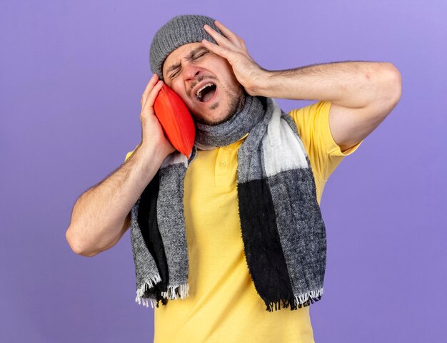 Aching young blonde ill slavic man wearing winter hat and scarf