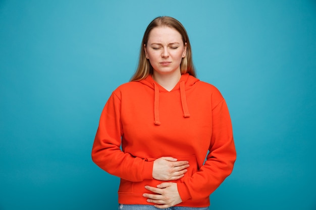 Aching young blonde woman keeping hands on belly with closed eyes 