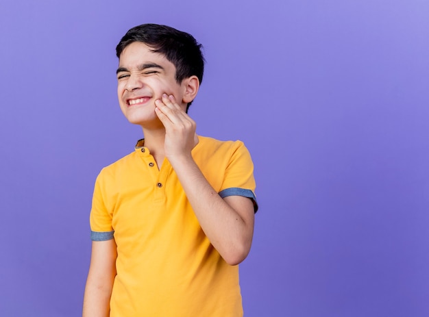 Free photo aching young caucasian boy touching cheek having toothache isolated on purple wall with copy space