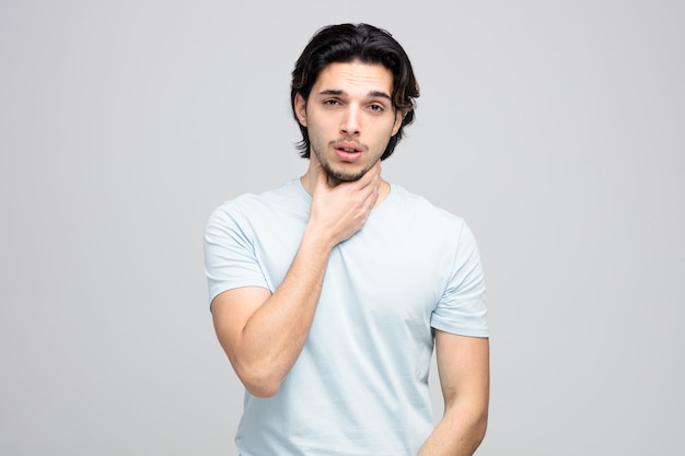 aching young handsome man looking at camera keeping hand on neck isolated on white background