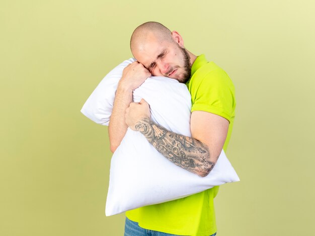 痛む若い病気の人は、オリーブグリーンの壁に隔離された枕に頭を抱えて置きます