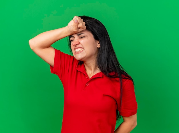 Aching young ill woman putting hand on head with closed eyes suffering from headache isolated on green wall with copy space