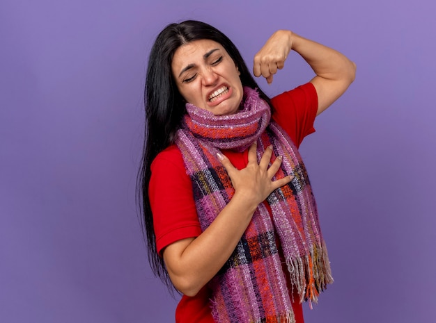 Sciarpa da portare della giovane donna ammalata dolorante che fa forte gesto che mette la mano sul petto con gli occhi chiusi isolati sulla parete viola