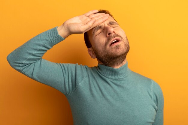 Aching young man putting hand on forehead with closed eyes suffering from headache isolated on orange wall