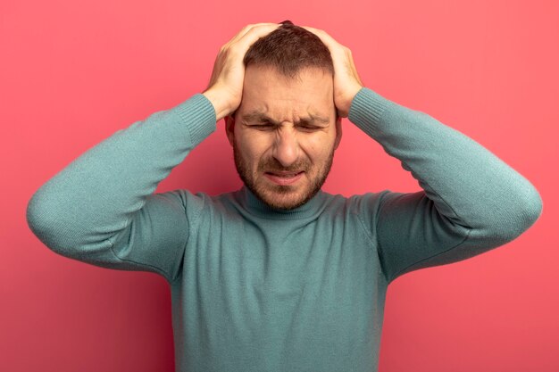 ピンクの壁に隔離された目を閉じて頭痛に苦しんで頭に手を置く痛む若い男