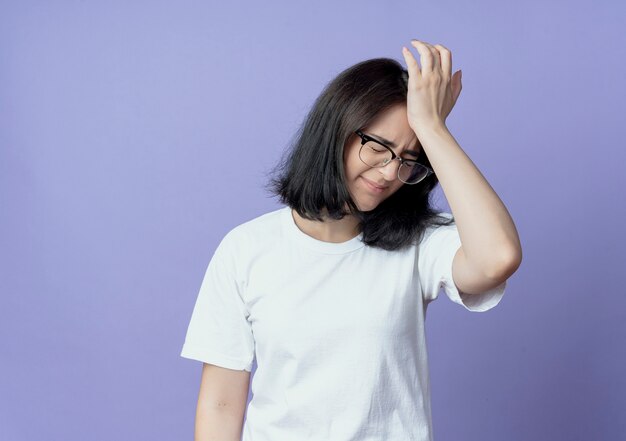 Aching young pretty caucasian girl wearing glasses putting hand on head suffering from headache with closed eyes isolated on purple background with copy space