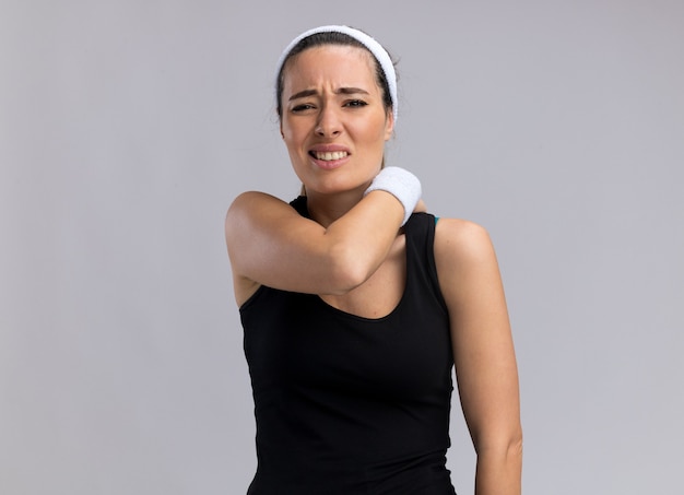 Aching young pretty sporty woman wearing headband and wristbands putting hand on back