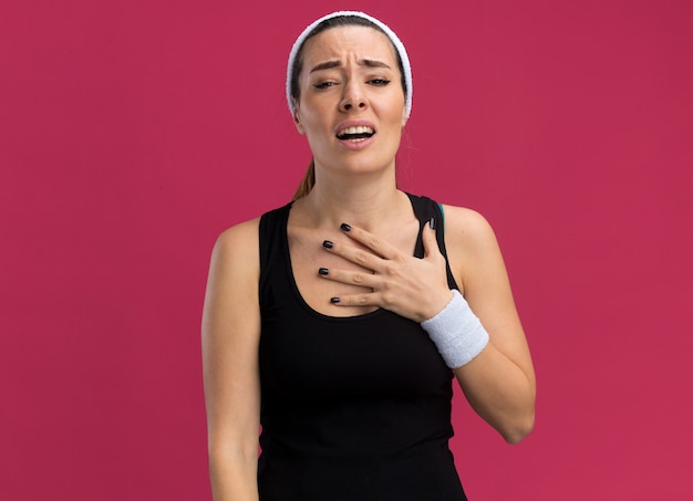Free photo aching young pretty sporty woman wearing headband and wristbands putting hand on chest