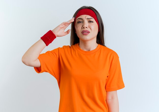 Aching young sporty woman wearing headband and wristbands looking touching head 