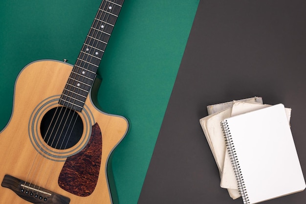 Acoustic guitar and empty notebook on a colored background top view