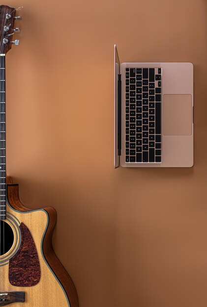 Acoustic guitar and laptop on a brown background top view copy space