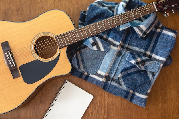 Acoustic guitar notebook and shirt on wooden background