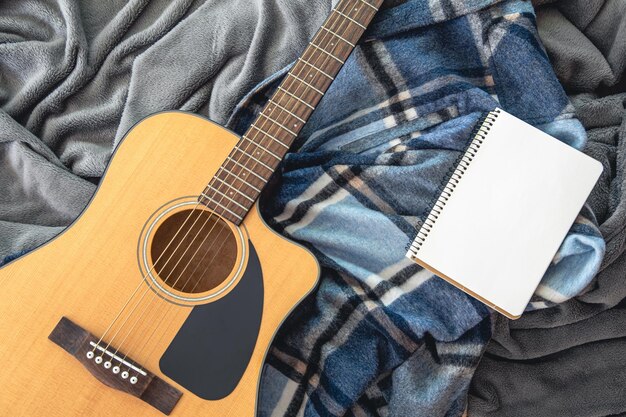 Acoustic guitar and notepad on a plaid background top view