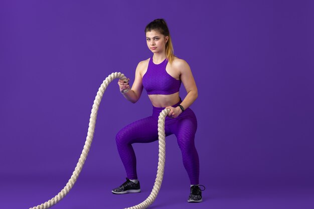 Active. Beautiful young female athlete practicing , monochrome purple portrait. Sportive caucasian fit model with ropes. Body building, healthy lifestyle, beauty and action concept.