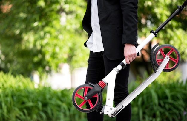 Активный бизнесмен, перевозящих скутер на открытом воздухе