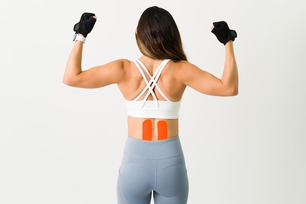 キネシオロジーテープを使用したアクティブな女性アスリート。強いトレーニングのために背中の下部にキネシオテープを付けたフィットした若い女性の背面図