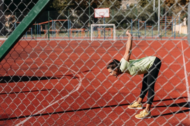 Active female in sport clothing stretching body outdoors