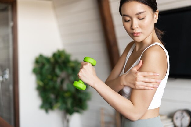 건강한 몸을 가진 활동적이고 건강한 아시아 소녀는 집에서 아령을 들고 운동을 하고 있습니다.