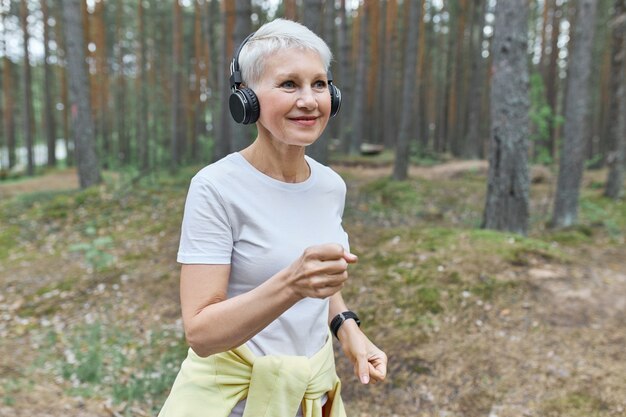 Active mature female runner in wearing sports clothes and wireless headphones, listening to music wearing headphones.