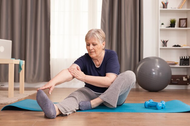 Active old woman exercising on the yoga mat in her comfortable apartment