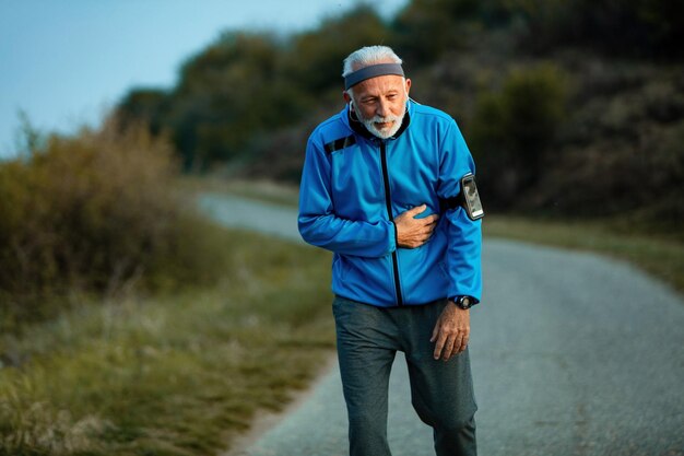 Active senior man getting out of breath while jogging in nature Copy space