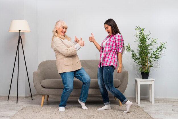 Active senior woman and her young daughter showing thumb up sign to each other in the living room