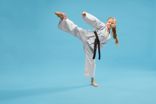 Active sporty girl in kimono kicking with leg in studio