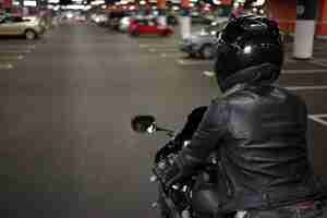 Free photo active way of life, motorcycling, night city and people concept. rear shot of fashionable confident female biker wearing safety helmet and black leather jacket, riding her motorbike on parking lot