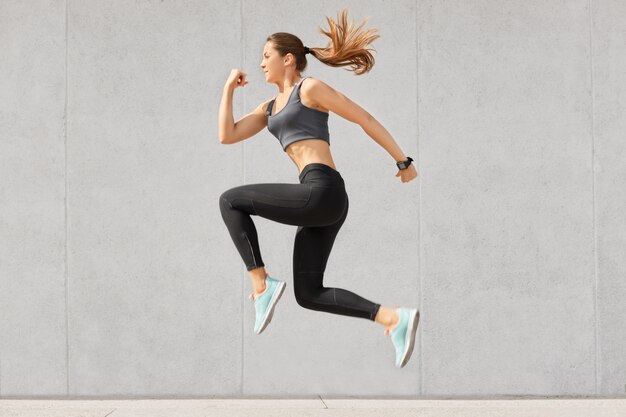 Активная женщина, полная энергии, прыгает высоко в воздухе, носит спортивную одежду, готовится к спортивным соревнованиям