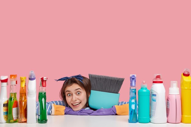 アクティブな女性は家の掃除を楽しんで、新しい洗浄剤を使用し、ほうきを運び、楽しく見え、汚れた表面をほこりを払い、注文に応じてフラットにします