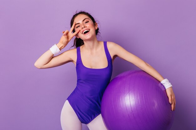 Active woman in sportswear in 80s style smiles and shows peace sign