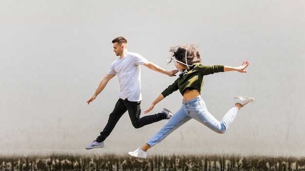 Active young couple jumping against grunge wall