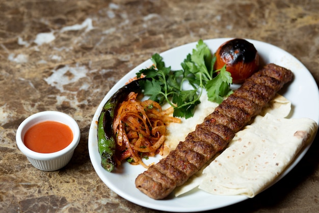 Adana kebab served with flatbread, grilled pepper and tomato and caramelized onion