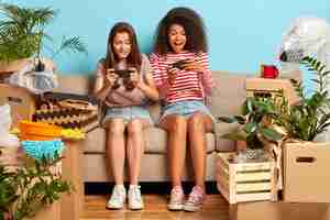 Free photo addicted girlfriends sitting on the couch with phones surrounded by boxes