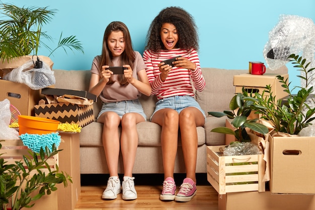 Addicted girlfriends sitting on the couch with phones surrounded by boxes