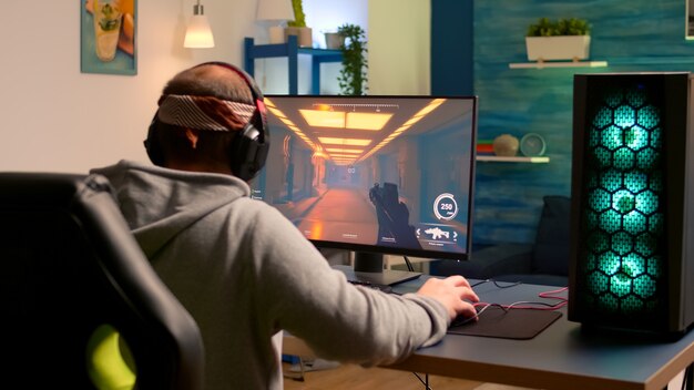 Addicted video game r performing cyber video games using professional headphones in gaming room. Competitive gamer playing video game tournament with new graphics on powerful computer.