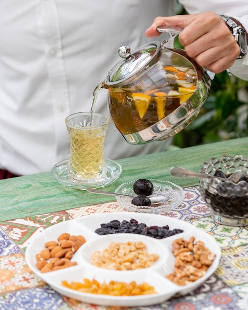 Adding fruit tea into glass with nuts around.