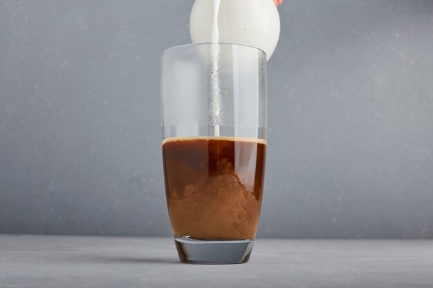 Adding milk to coffee in a glass. 