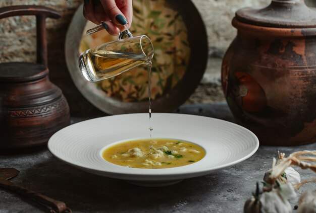 Adding olive oil to chicken broth soup.