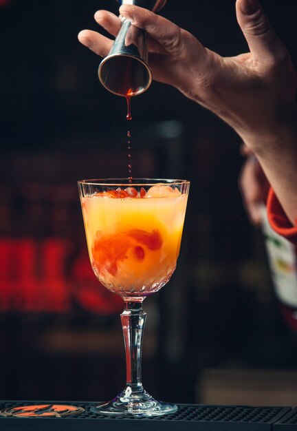 Adding red syrup into orange cocktail.