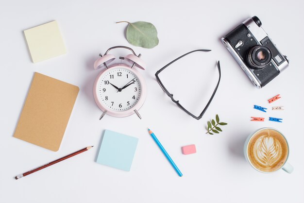 Adhesive notes; pencils; rubber; eyeglasses; camera and cappuccino cup with latte art on white background