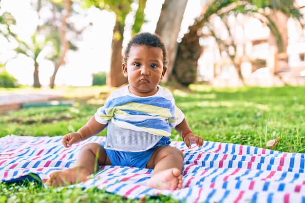 Free photo adorable african american toddler sitting on the grass at the park.