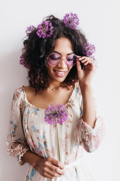 Adorable african girl with curly hairstyle holding allium. black lady in sunglasses posing with purple flowers.