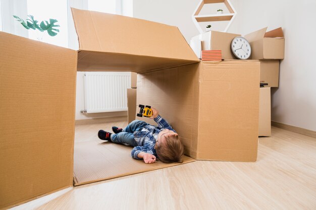 Adorable baby boy lying in the cardboard box playing with toy car at home