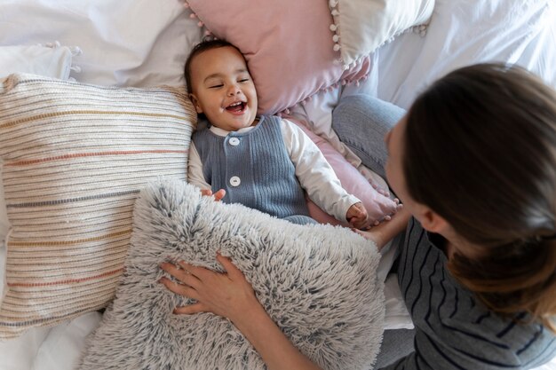 Adorable baby laughing and playing with his mother on bed
