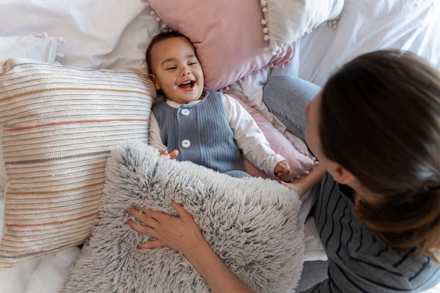 Прелестный ребенок смеется и играет со своей матерью на кровати